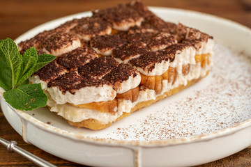 Tiramisu. Traditional italian dessert on wooden background. Garnished with a sprig of mint, lime slices. In a transparent cup, tea with sea buckthorn.