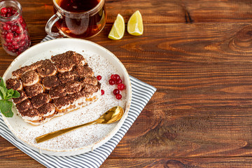 Tiramisu. Traditional italian dessert on wooden background. Garnished with a sprig of mint, lime slices. In a transparent cup, tea with sea buckthorn.