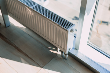 white radiator battery in the office near the window. - obrazy, fototapety, plakaty