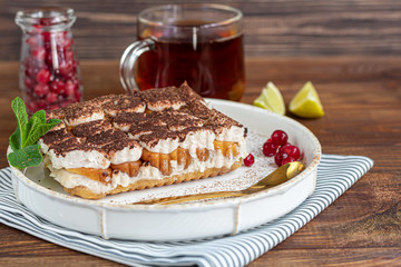 Tiramisu. Traditional italian dessert on wooden background. Garnished with a sprig of mint, lime slices. In a transparent cup, tea with sea buckthorn.
