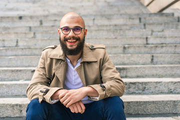 Happy young man looking at camera while sitting on stairs and smiling