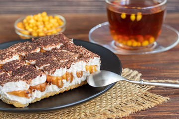 Tiramisu. Traditional italian dessert on wooden background. Garnished with a sprig of mint, lime slices. In a transparent cup, tea with sea buckthorn.