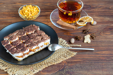 Tiramisu. Traditional italian dessert on wooden background. Garnished with a sprig of mint, lime slices. In a transparent cup, tea with sea buckthorn.