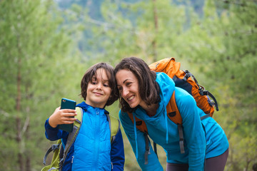 A child with a backpack takes a selfie on a smartphone with mom on the background of a mountain forest.