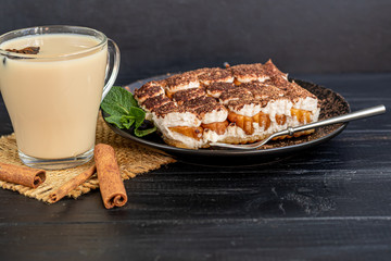 Tiramisu. Traditional italian dessert on wooden background. Garnished with a sprig of mint, lime slices. In the background are drinks. Coffee, masala tea with spices.