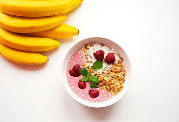 pink smoothie with granola and raspberries and bananas on a white background