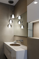 Stylish brown sink, chrome faucet, large mirror and ceiling light three-lamp chandelier. Modern bathroom design.