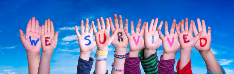 Children Hands Building Colorful English Word We Survived. Blue Sky As Background