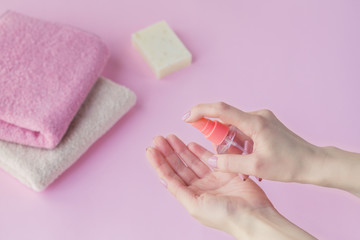 Female hand using antibacterial hand sanitizer on light pink background.