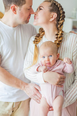 Beautiful young parents are holding their little newborn daughter in their arms. Blue-eyed little girl of 2 months. Baby
