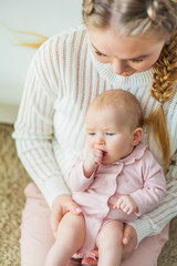 A beautiful young mother holds in her arms a small pretty blue-eyed 2-month-old daughter. Newborn.