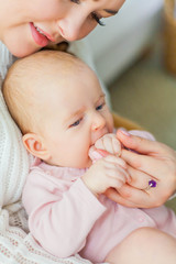 Close-up. A beautiful young mother holds in her arms a small pretty blue-eyed 2-month-old daughter. Newborn.