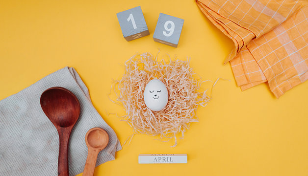 country style Easter banner. cute Easter egg with a black marker drawn face in a paper nest made of pressed paper, gray wooden cubes with the date of Easter April 19, cotton napkins and wooden spoons