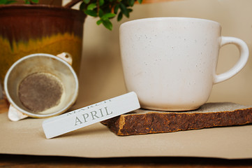 white Cup on a natural stand made of gray stone with a home green plant and a wooden perpetual calendar that says the month of April