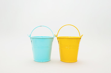 Blue metal minature bucket and yellow metal bucket with raised handles on a white background