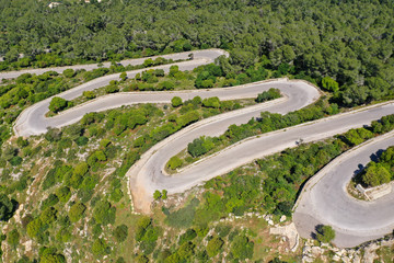 Aerial view of a narrow winding mountain road surrounded by lush green nature.