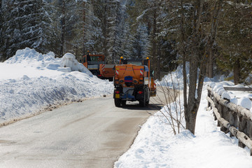 Orange-coloured Snowplough Operating on the Road with Snow on the Edges