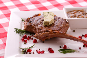 Rack of lamb served with pomegranate seeds and sauce on white plate over red plaid tablecloth. Italian concept.