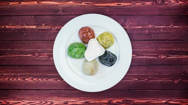 Plate with colored oriental dumplings and sauces rotates on wooden background. Top view