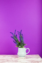 Lavender flowers in a mug on a marble table and purple background