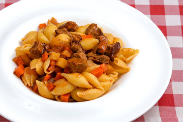 Macaroni pasta with meat pieces in tomato sauce and vegetables in bowl. Top view.