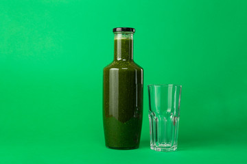 Fresh celery spinach juice in a glass bottle and an empty glass near isolated on green background. Healthy eating Detox juice diet.