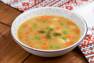 Chicken soup with noodles and vegetables served in white bowl over rustic wooden table with traditional tablecloth.
