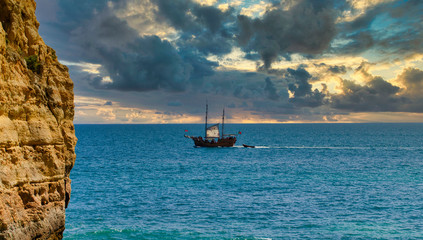 Pirate boat in Carvoeiro, Algarve, Portugal.  Beautiful sunset. Part of a cliff in the foreground. ...