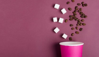 Closeup of pink cup, coffee beans, sugar cubes on the dark red surface.Empty space for design.Preparing delicious classic coffee concept