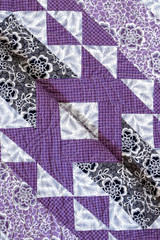 Purple coloured handmade patchwork bed quilt with various fabric geometric designs