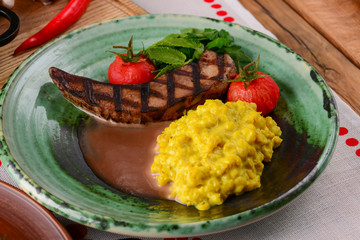 Grilled steak with gravy and vegetables served on a green plate over traditional Ukrainian tablecloth.