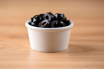 Black olives served in a small little white bowl over light rustic wooden background.