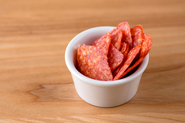Salami pieces sliced in a little small white bowl. Beer snack. Appetizer. Light rustic wooden background.