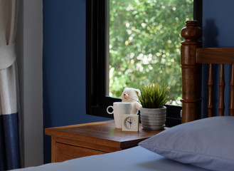A teddy bear,coffee cup and white alarm on wood table in blue bedroom