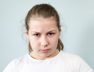 Caucasian pre-teen girl with frowning eyebrows and heavy look, angry young child, grey background,...