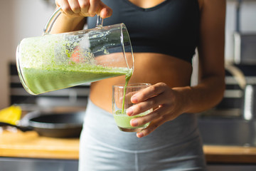 Healthy fitness diet concept. Sporty woman serving a green detox smoothie for breakfast in the kitchen. - 338719448