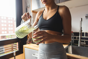 Healthy fitness diet concept. Sporty woman serving a green detox smoothie for breakfast in the...