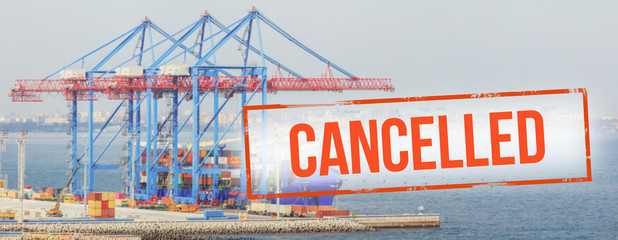 Red inscription "cancelled" on a blurred background of container ship  in cargo port. Concept: Global economic crisis, reduction of trade, suspension of carriage, halting production due to a pandemic