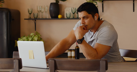 Hispanic male having a conversation during video call with colleagues, kitchen background. Quarantine working, stay home, coronavirus pandemic.