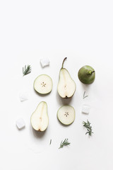 Green whole and sliced pear fruit, melting ice cubes and rosemary herbs leaves, branches isolated on white table background. Summer refreshment concept. Flat lay, top view, vertical. Empty copy space