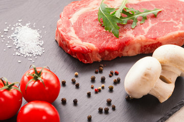 Raw ribeye beef steak with spices, Black Angus meat with seasonings, gray stone background