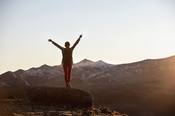 Happy female hiker stands with raised arms in mountains