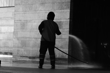 silhouette of a man or woman in working uniform cleaning square with water during the quarantine of epidemic coronavirus