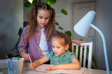 older sister helps younger with their writings