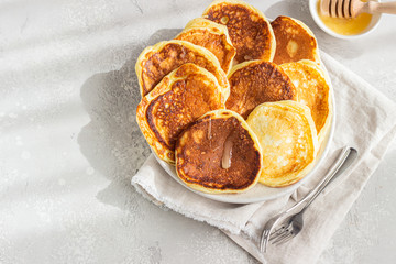 Homemade pancakes with honey and sour cream, sunny shadowed table surface. Light grey concrete background. Natural light and shadows food photography concept. Breakfast.