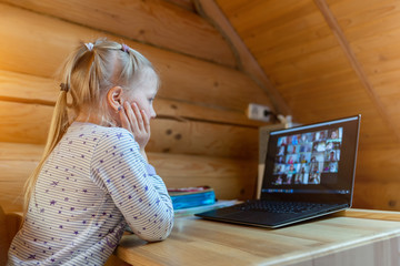 Cute adorable caucasian little blond girl sitting at desk with laptop during online video chat school lesson session with teacher and class. Remote education concept. Self-isolation at quarantine