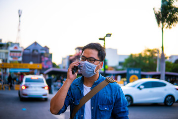 Concept, diseases, viruses, allergies, air pollution. Man wearing surgical mask on street while using phone. The image face of a young man wearing a mask to prevent germs, toxic fumes, and dust. 