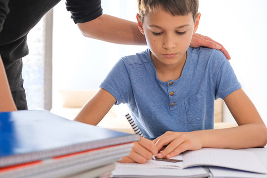 Kid Sitting At The Table With Many Books Notebooks And Doing Homework. Mother Helping Him. Learning Difficulties, Learning At Home, Education, Motivation Concept