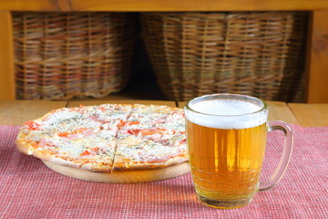 The mug of light beer on the background of pizza with cheese and tomatoes. 