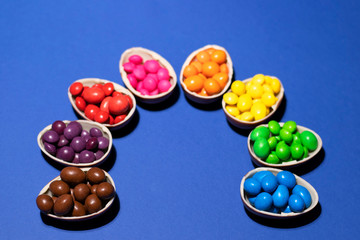 A semicircle of halves of chocolate eggs in each of which is colored jelly. The photo was taken close with shadows on a deep blue color. There is a place for text.
